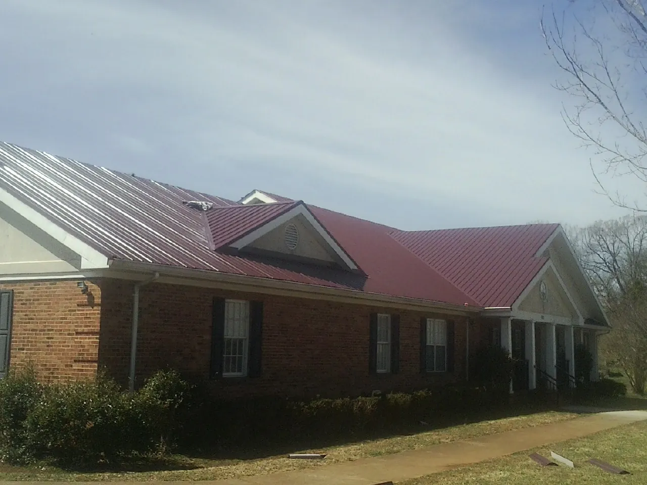 Red metal roof with gabled entries on a long brick building, from a Hail Damage Roof Repair job in Stillwater